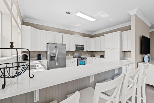 kitchen with sink, white cabinetry, appliances with stainless steel finishes, a kitchen breakfast bar, and kitchen peninsula