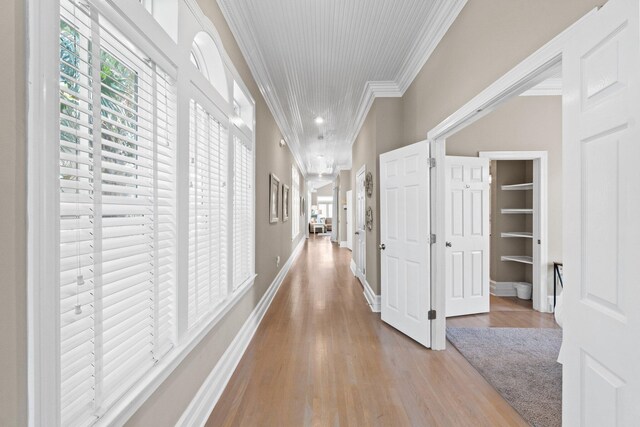 corridor featuring built in features, ornamental molding, and light hardwood / wood-style floors