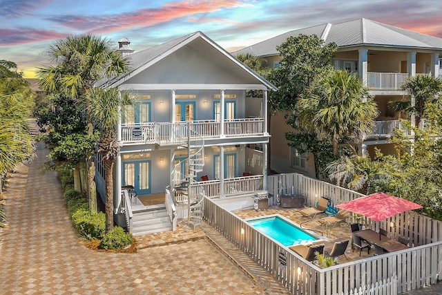 back house at dusk with a balcony, a fenced in pool, and a patio area