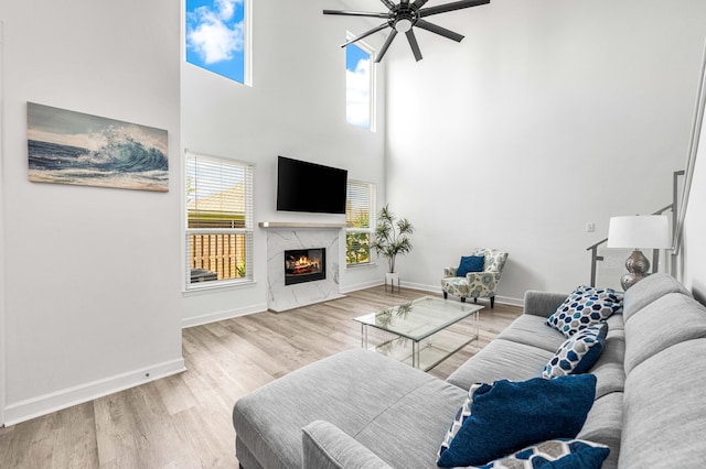 living room with ceiling fan, a premium fireplace, a high ceiling, and light hardwood / wood-style floors