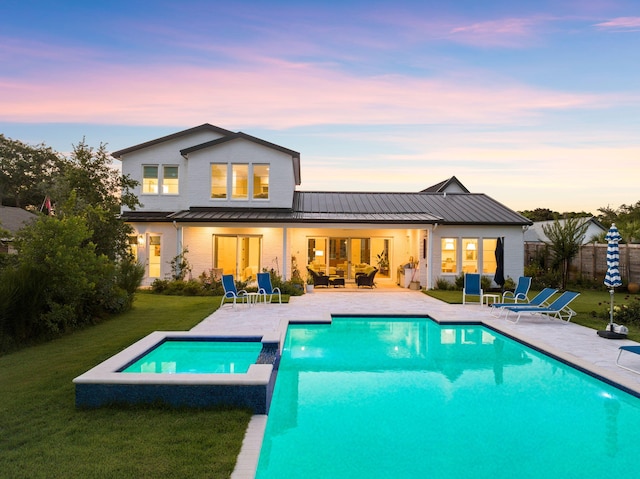 back house at dusk with a patio and a lawn