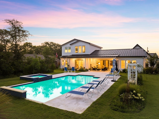 pool at dusk with an in ground hot tub, a yard, and a patio area