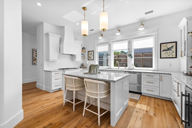 kitchen featuring white cabinets, custom range hood, a kitchen breakfast bar, light hardwood / wood-style floors, and a kitchen island