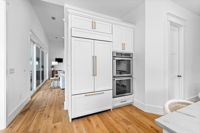 kitchen with light stone countertops, light wood-type flooring, stainless steel double oven, and paneled built in refrigerator