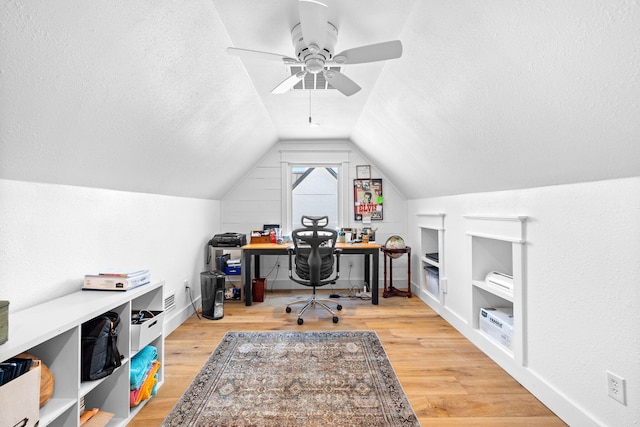 home office with a textured ceiling, lofted ceiling, light hardwood / wood-style floors, built in shelves, and ceiling fan