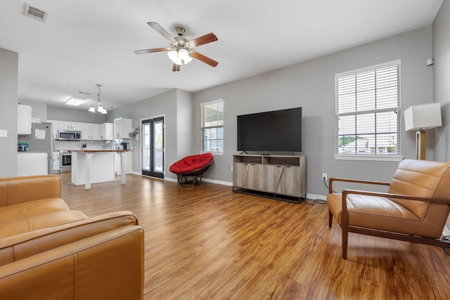living area featuring ceiling fan with notable chandelier, light wood finished floors, visible vents, and baseboards