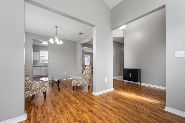 living area with a chandelier, wood finished floors, visible vents, and baseboards