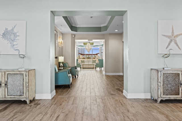 corridor with light wood-style floors, a raised ceiling, crown molding, and baseboards