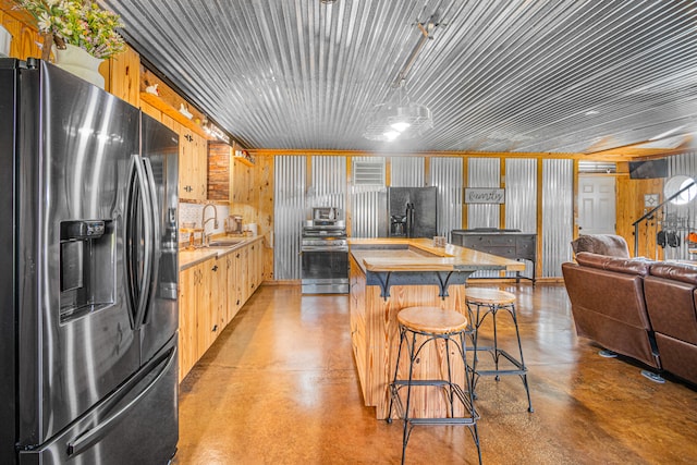 kitchen with sink, black fridge, stainless steel range oven, wooden walls, and refrigerator with ice dispenser