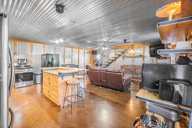 kitchen with appliances with stainless steel finishes, ceiling fan, concrete floors, and a kitchen island