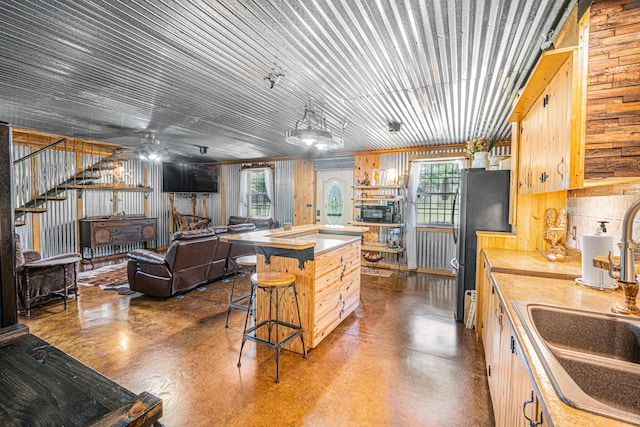 kitchen with sink, a center island, black refrigerator, light brown cabinets, and ceiling fan