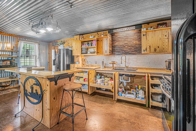 kitchen featuring stainless steel refrigerator with ice dispenser, black fridge, a breakfast bar, sink, and decorative light fixtures