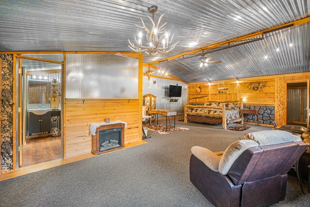 carpeted living room with ceiling fan with notable chandelier, a fireplace, wood walls, and lofted ceiling