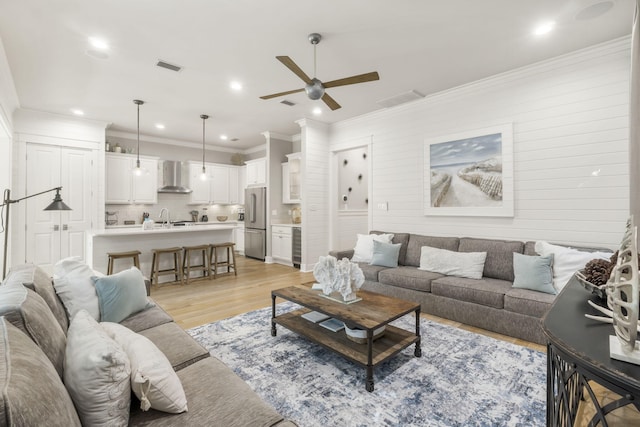 living room featuring ceiling fan, ornamental molding, sink, and light wood-type flooring