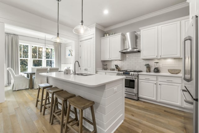 kitchen with wall chimney exhaust hood, sink, white cabinetry, a center island with sink, and appliances with stainless steel finishes