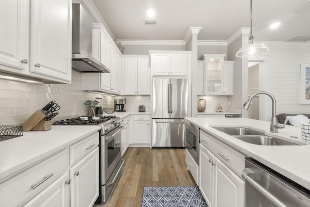 kitchen featuring wall chimney range hood, sink, appliances with stainless steel finishes, white cabinets, and decorative light fixtures