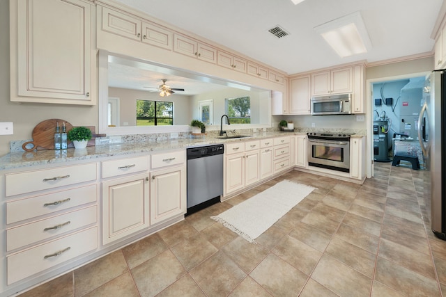 kitchen with appliances with stainless steel finishes, sink, ceiling fan, light stone counters, and cream cabinets