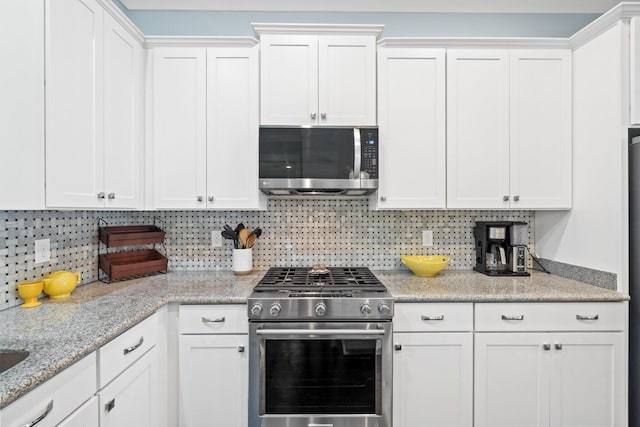 kitchen with white cabinetry, backsplash, stainless steel appliances, and light stone countertops