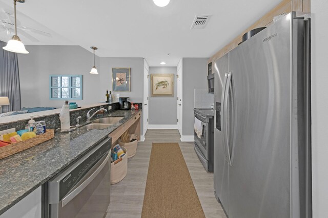 kitchen with hanging light fixtures, dark stone countertops, stainless steel appliances, sink, and wood-type flooring