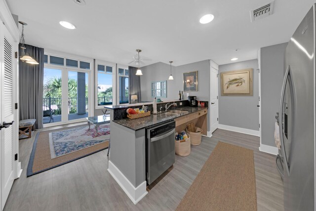 kitchen with appliances with stainless steel finishes, dark stone counters, light hardwood / wood-style flooring, kitchen peninsula, and decorative light fixtures