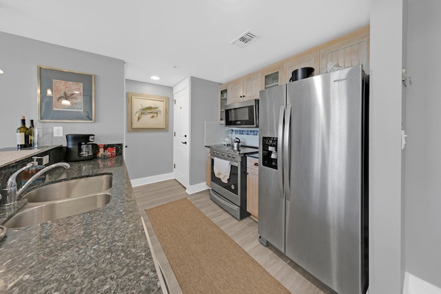 kitchen featuring light hardwood / wood-style flooring, light brown cabinetry, appliances with stainless steel finishes, dark stone counters, and sink