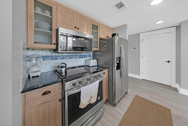 kitchen featuring decorative backsplash, light brown cabinetry, dark stone counters, light hardwood / wood-style floors, and stainless steel appliances