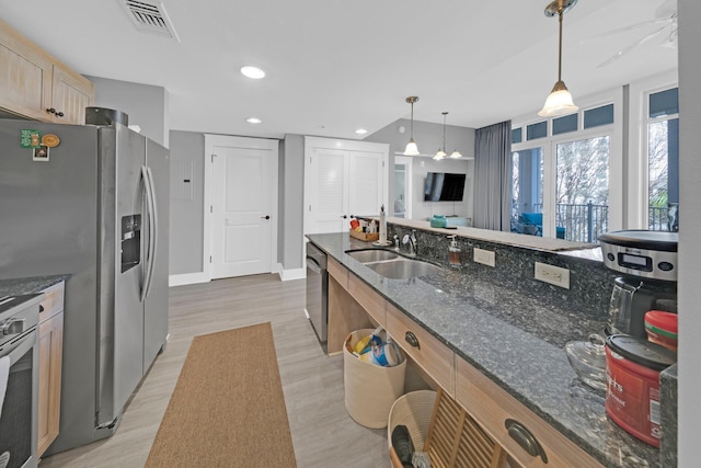 kitchen featuring light hardwood / wood-style flooring, appliances with stainless steel finishes, dark stone counters, hanging light fixtures, and sink