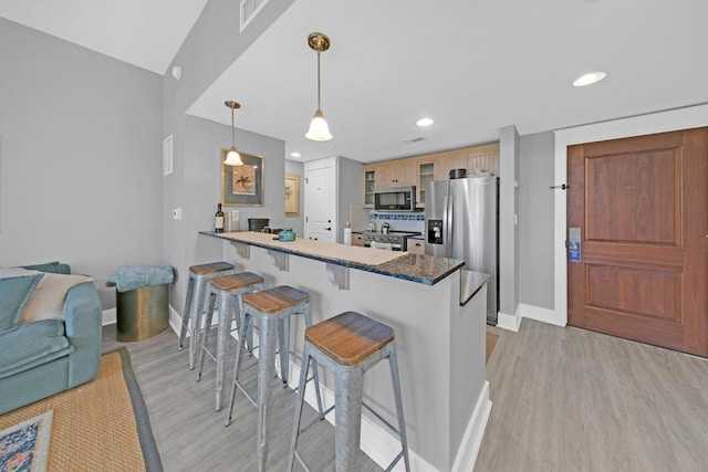 kitchen with appliances with stainless steel finishes, kitchen peninsula, light wood-type flooring, and a breakfast bar