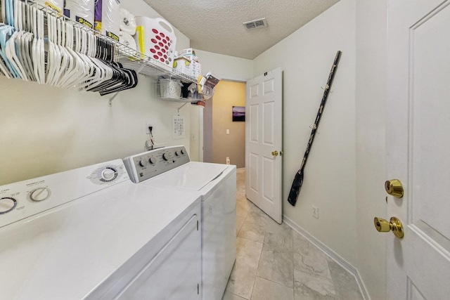 clothes washing area with a textured ceiling, independent washer and dryer, and light tile patterned floors