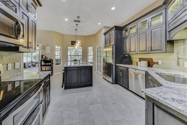 kitchen featuring sink, decorative light fixtures, appliances with stainless steel finishes, decorative backsplash, and light stone countertops