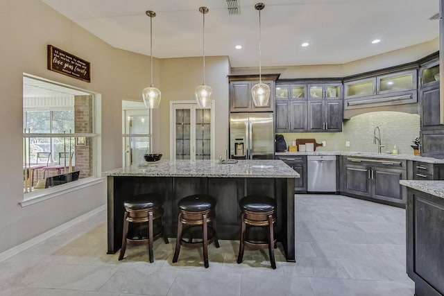 kitchen with stainless steel appliances, decorative backsplash, light stone countertops, a center island, and hanging light fixtures