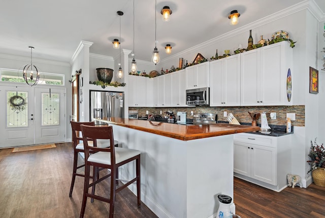 kitchen featuring butcher block countertops, backsplash, white cabinets, hanging light fixtures, and stainless steel appliances