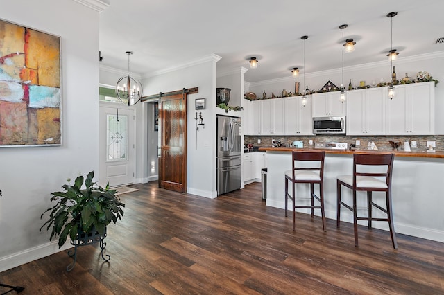 kitchen with pendant lighting, appliances with stainless steel finishes, white cabinets, a kitchen bar, and a barn door