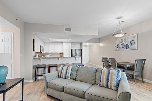 living area with light wood-type flooring, visible vents, and baseboards