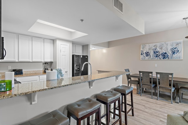 kitchen featuring visible vents, stone countertops, white cabinetry, black appliances, and a kitchen breakfast bar