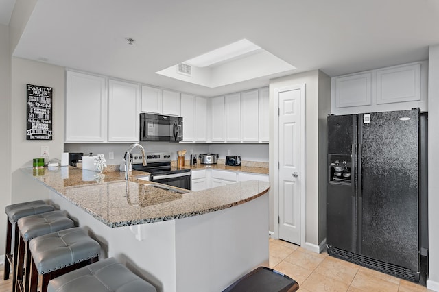 kitchen with light tile patterned flooring, light stone countertops, kitchen peninsula, black appliances, and white cabinets