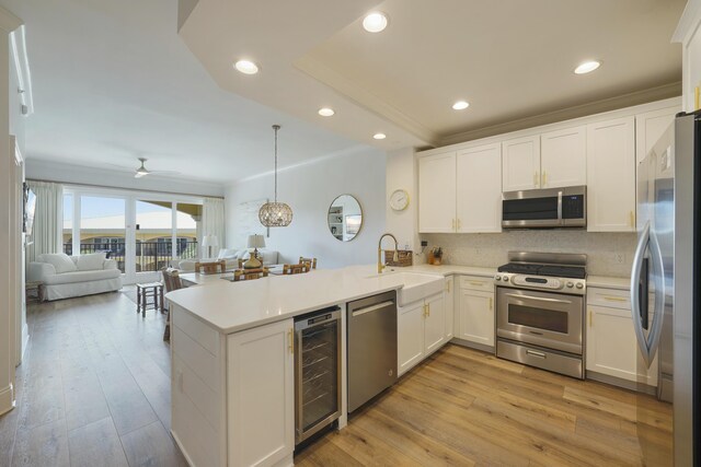 kitchen with appliances with stainless steel finishes, light wood-type flooring, beverage cooler, and kitchen peninsula