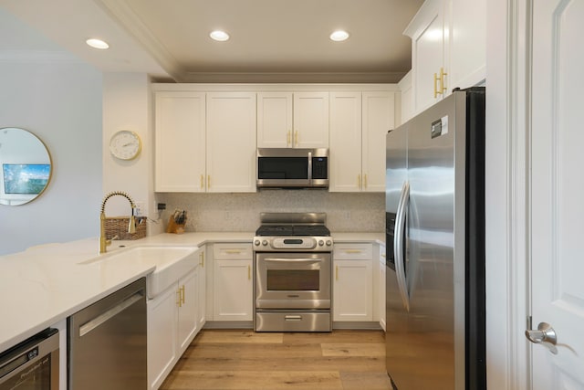 kitchen with appliances with stainless steel finishes, sink, light wood-type flooring, and white cabinets