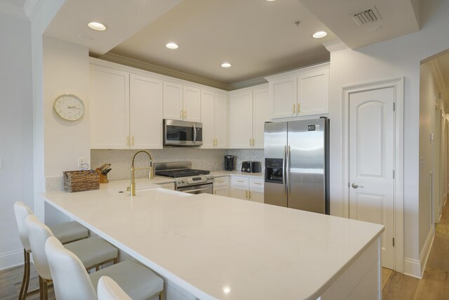 kitchen featuring decorative backsplash, kitchen peninsula, light wood-type flooring, stainless steel appliances, and a breakfast bar area