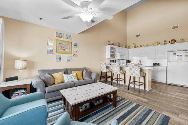 living room with light hardwood / wood-style floors, a towering ceiling, and ceiling fan