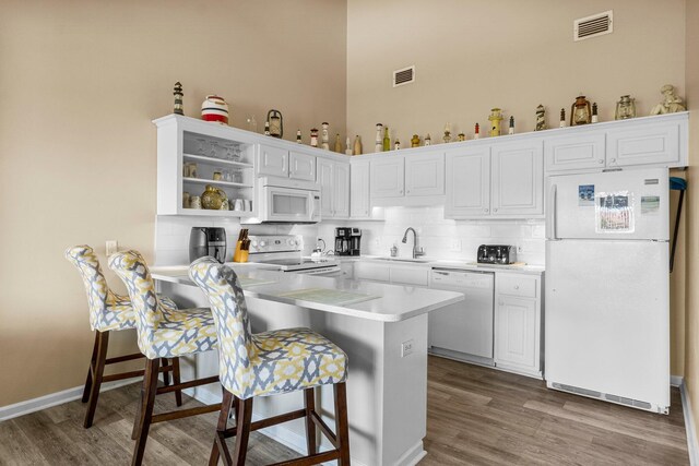 kitchen with white appliances, hardwood / wood-style floors, white cabinetry, and tasteful backsplash