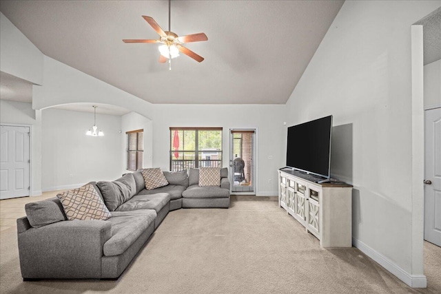 carpeted living room with high vaulted ceiling and ceiling fan with notable chandelier