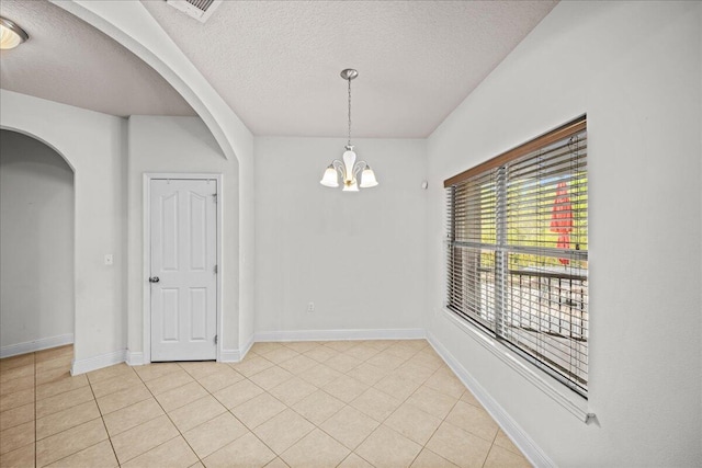 empty room with light tile patterned flooring, a textured ceiling, and an inviting chandelier