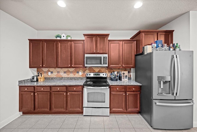 kitchen with a textured ceiling, light stone counters, appliances with stainless steel finishes, light tile patterned floors, and backsplash