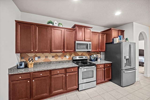 kitchen with stainless steel appliances, a textured ceiling, light stone countertops, light tile patterned flooring, and tasteful backsplash