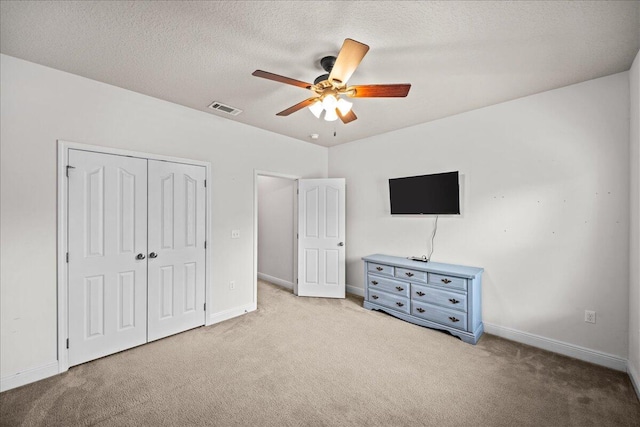 unfurnished bedroom featuring ceiling fan, a textured ceiling, light carpet, and a closet