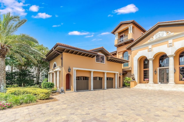 mediterranean / spanish-style house with a balcony, a tiled roof, decorative driveway, an attached garage, and stucco siding