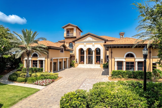 mediterranean / spanish house with stucco siding, a balcony, a tiled roof, decorative driveway, and a garage