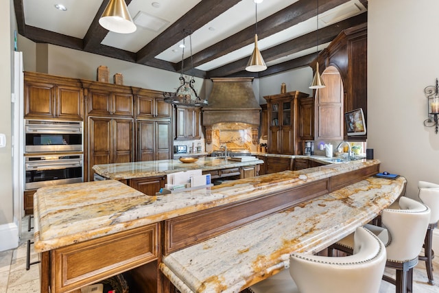 kitchen featuring custom range hood, decorative light fixtures, a large island, light stone counters, and beamed ceiling