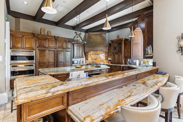 kitchen with custom range hood, a kitchen island, a sink, light stone counters, and beamed ceiling
